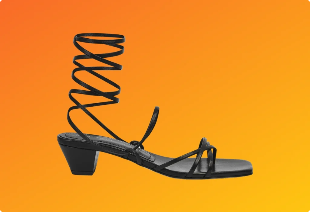 Black strappy sandal with block heel and ankle wrap displayed on an orange background